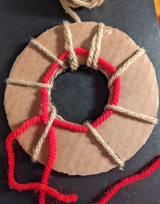 Mae gwlân brown wedi ei ddolennu o gwmpas y donut ar 8 pwynt gwahanol i ddal y llinyn clymu yn ei le. Mae'r llinyn clymu yn dilyn y cardfwrdd o gwmpas y ddolen gan groesi drosodd cyn gadael y pennau yn hongian dros yr ymyl i'w clymu ynghyd yn nes ymlaen