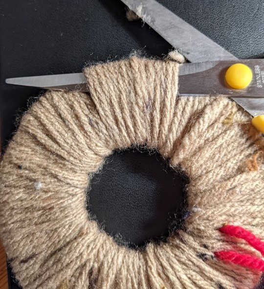 Mae'r siswrn rhwng y gwlân a'r cerdyn ar un ochr i'r donut. Mae mewn sefyllfa i ddechrau torri'r gwlân o gwmpas yr holl ymyl allanol.